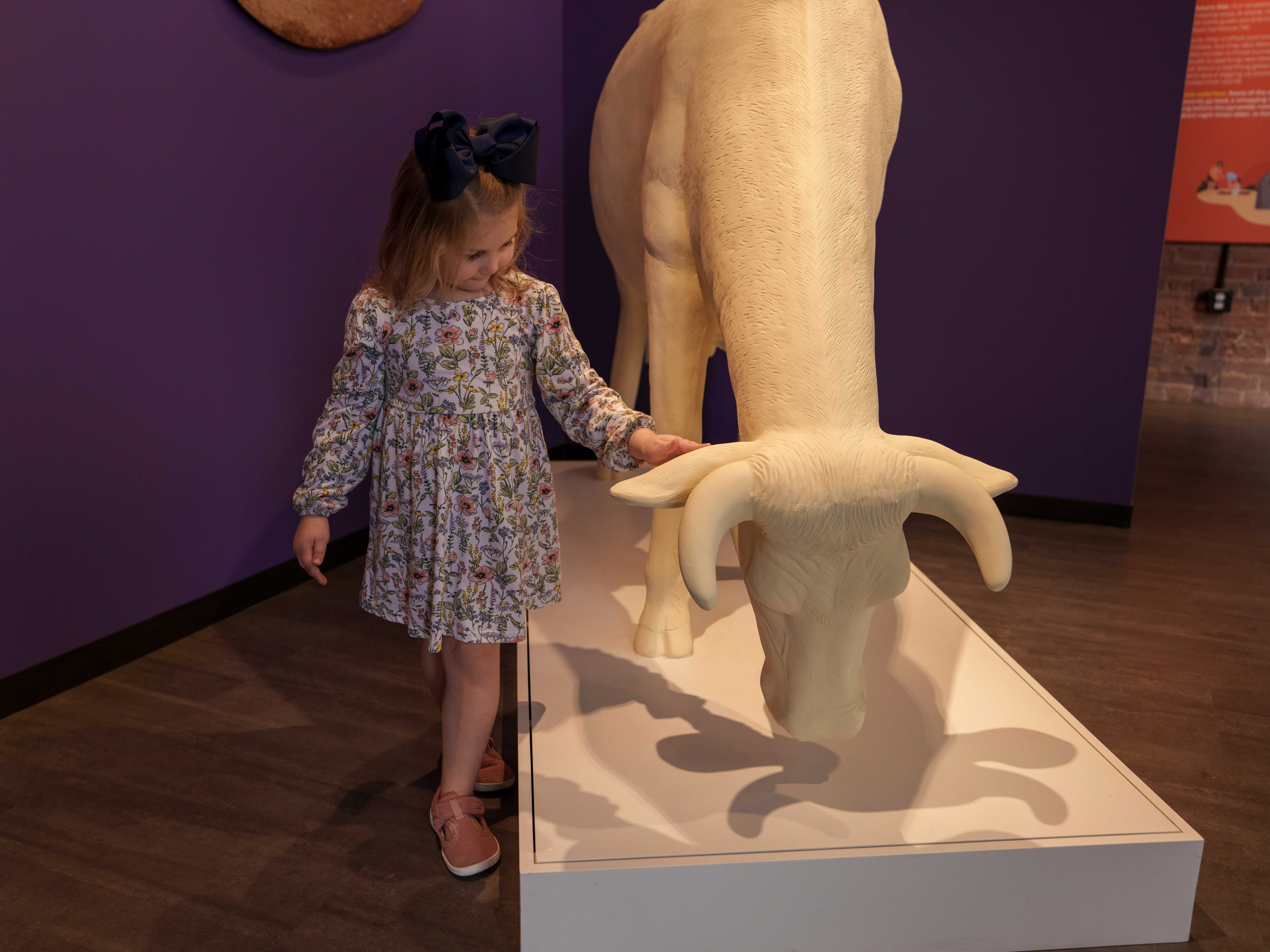 A young girl in a floral dress reaches out to gently touch a sculpture of a cow currency at the MoFun.