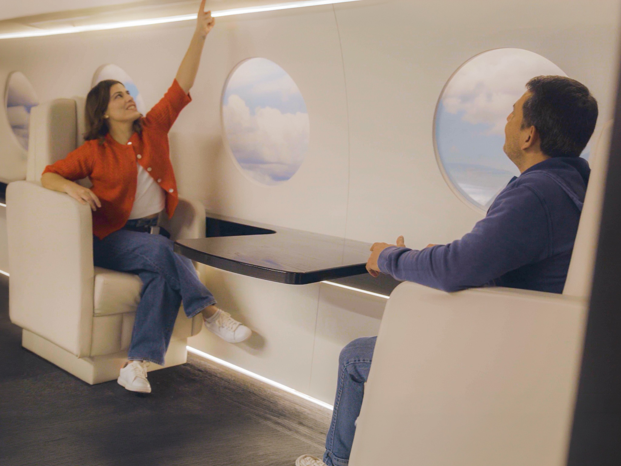Couple at a sleek table in MoFun's private jet exhibit, with painted clouds visible in the round windows behind them.