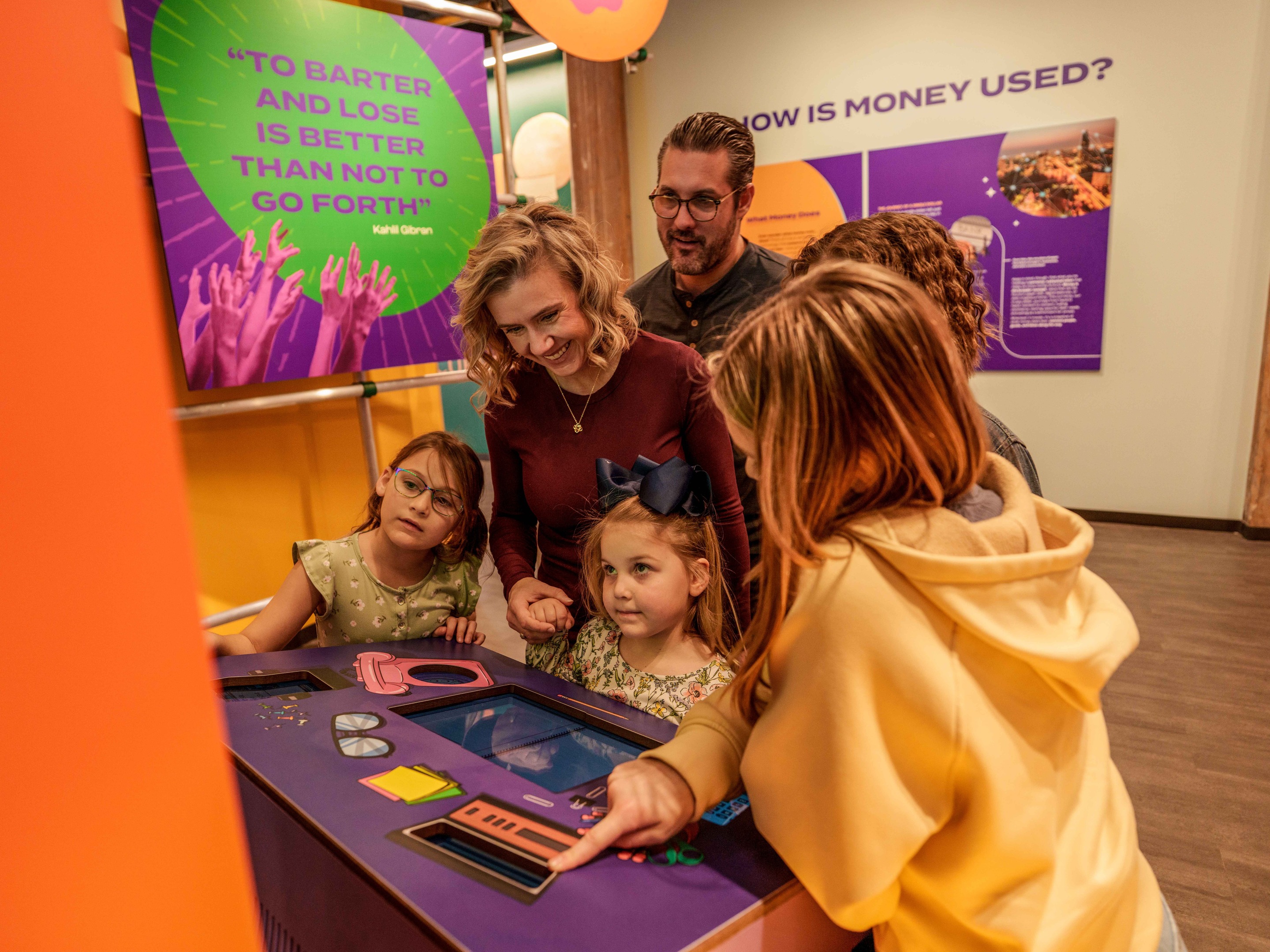 Family with children gathered around MoFun's interactive barter exhibit, smiling and pointing as they play to win.
