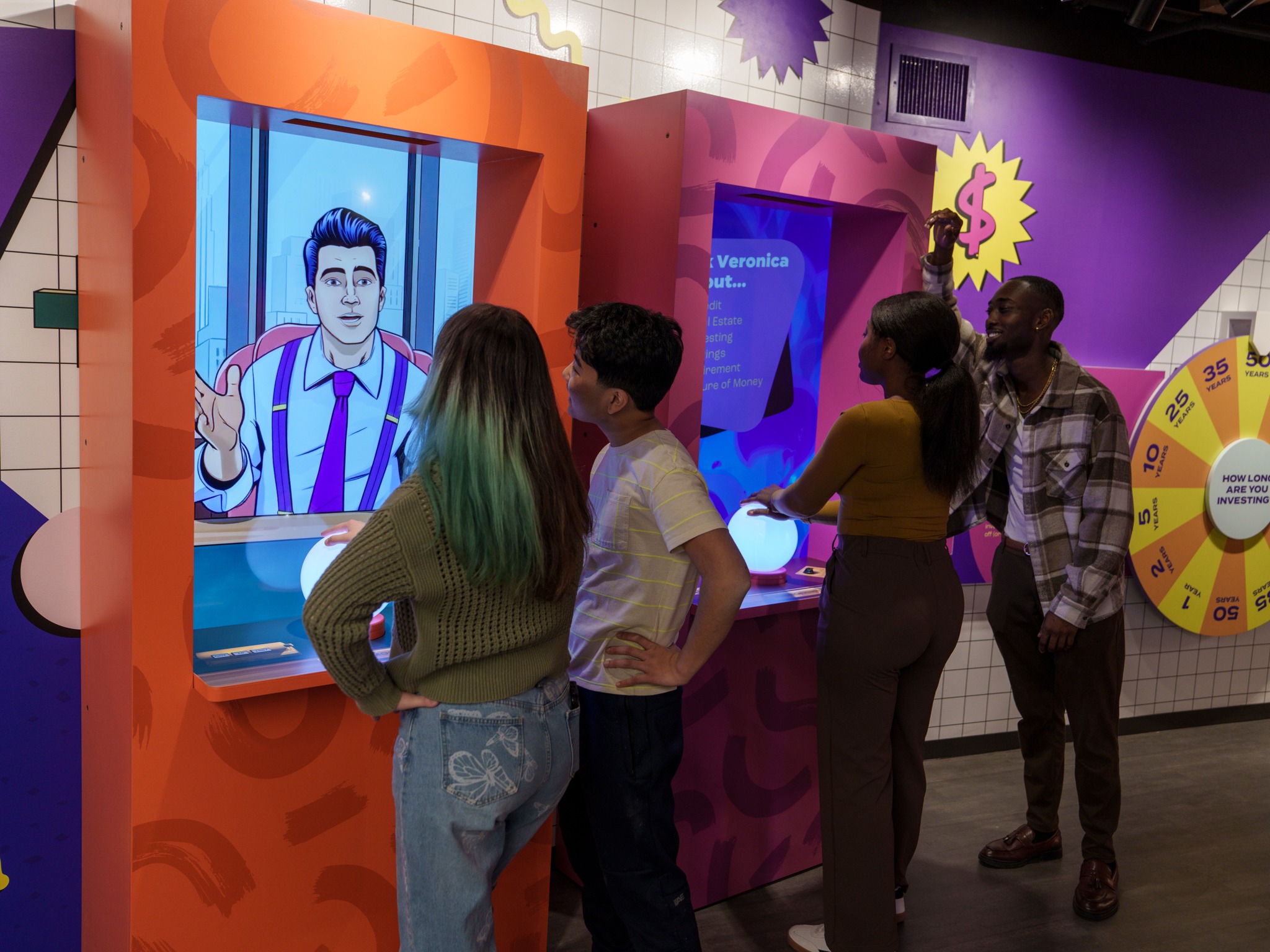 A small group of young professionals gathers around a colorful interactive money-investment exhibit at the MoFun.